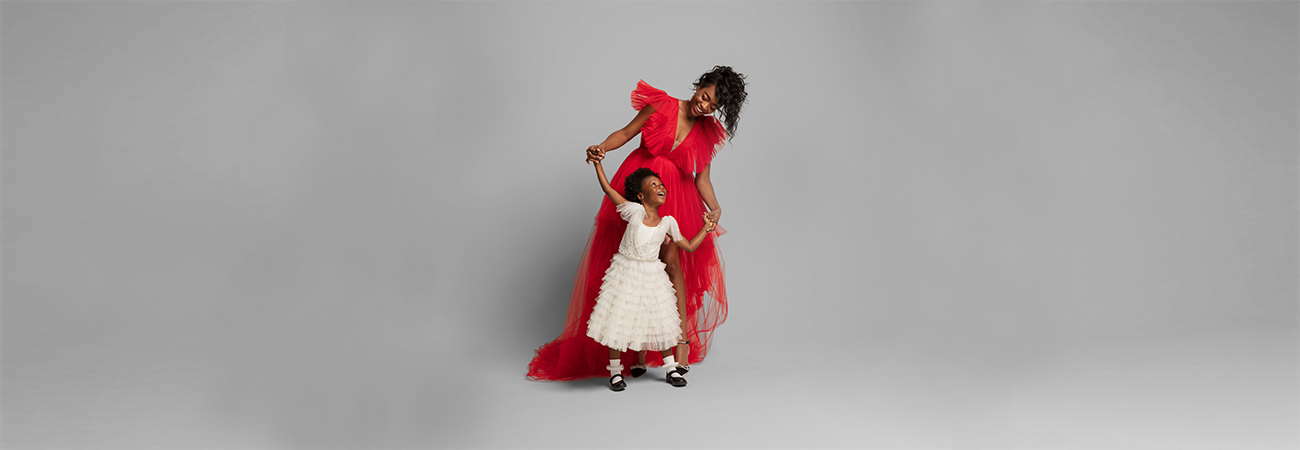 A mom in a red holiday dress dancing with her young daughter in a ruffled white dress