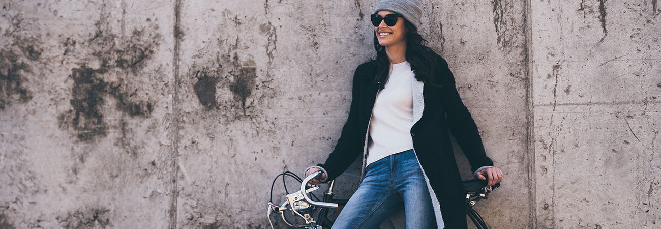 A smiling young woman standing with her bike in front of a cement wall