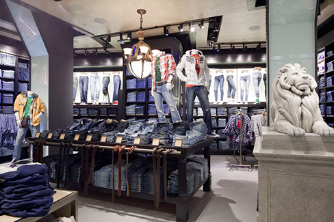 Interior of a denim clothing store featuring folded jeans, mannequins wearing casual outfits, wall displays of denim apparel, and a decorative lion statue near the entrance.