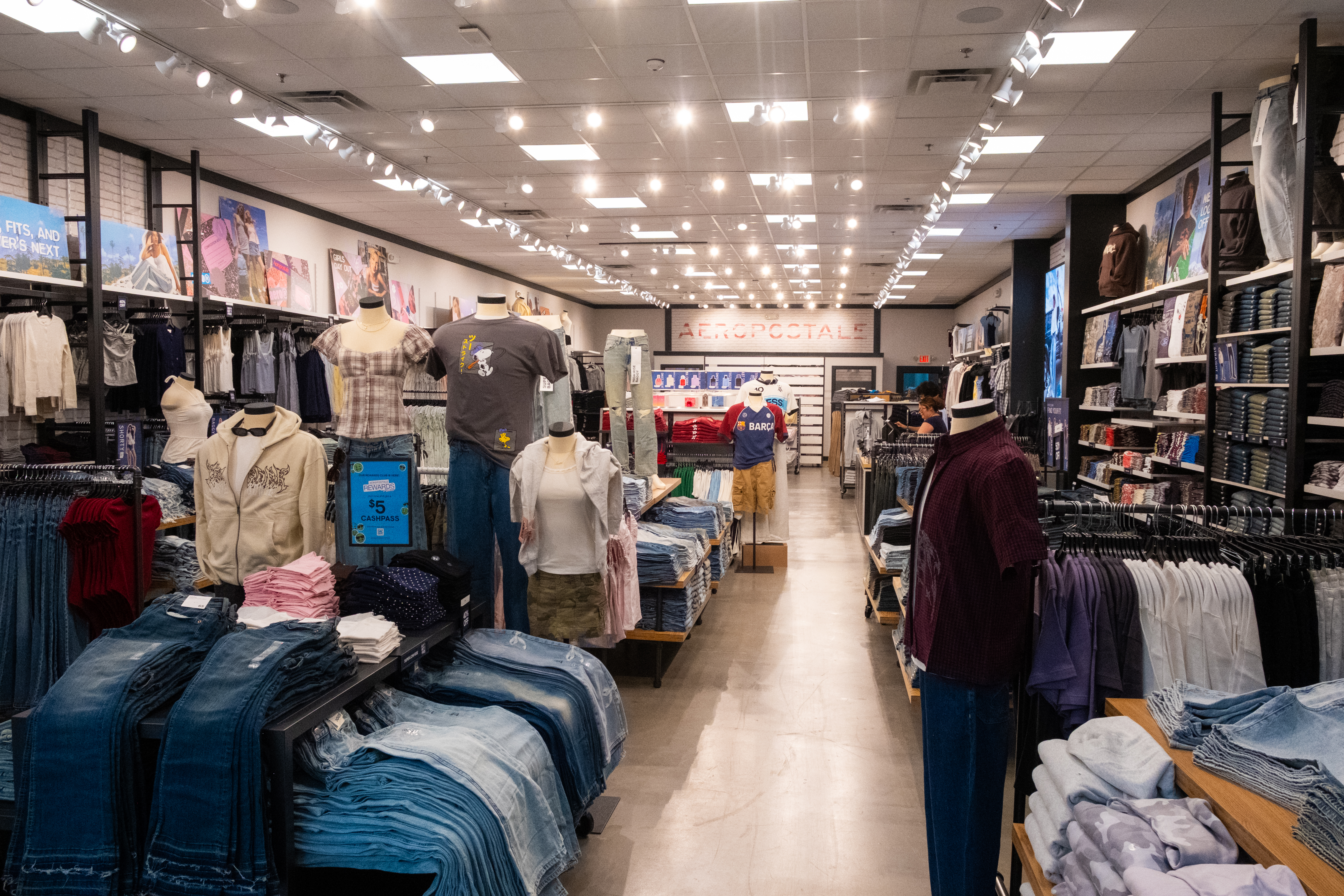 Interior of a denim clothing store featuring folded jeans, mannequins wearing casual outfits, wall displays of denim apparel, and a decorative lion statue near the entrance.