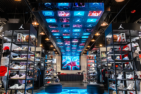 Inside DTLR sneaker and sportswear store, showcasing shoe displays, apparel racks, and a large illuminated digital ceiling feature.