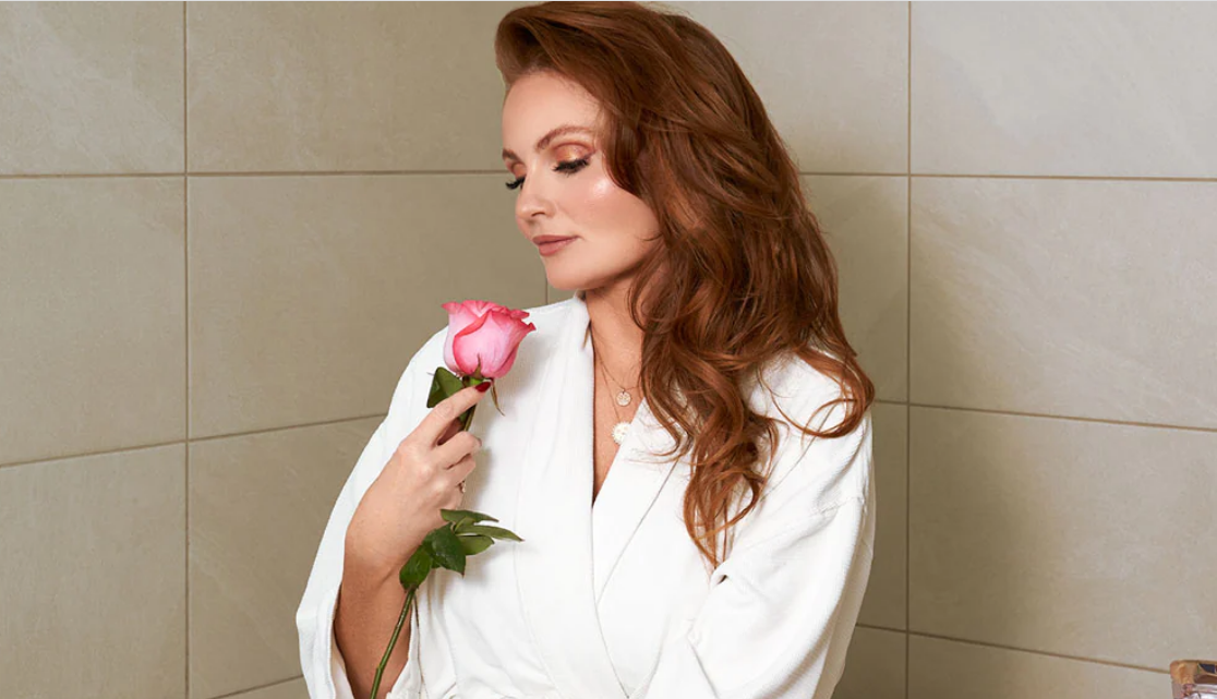 Woman in bathrobe sitting on tub with pink rose