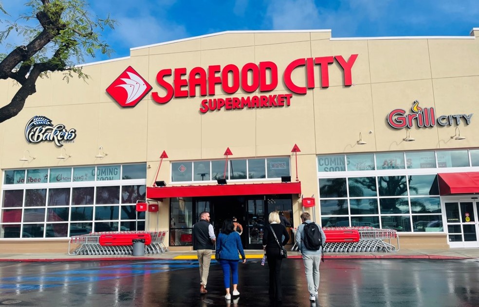 Sefood City Supermarket store main entrance with people walking inside. Bakers logo and Grill City logo on the outside of the store. 