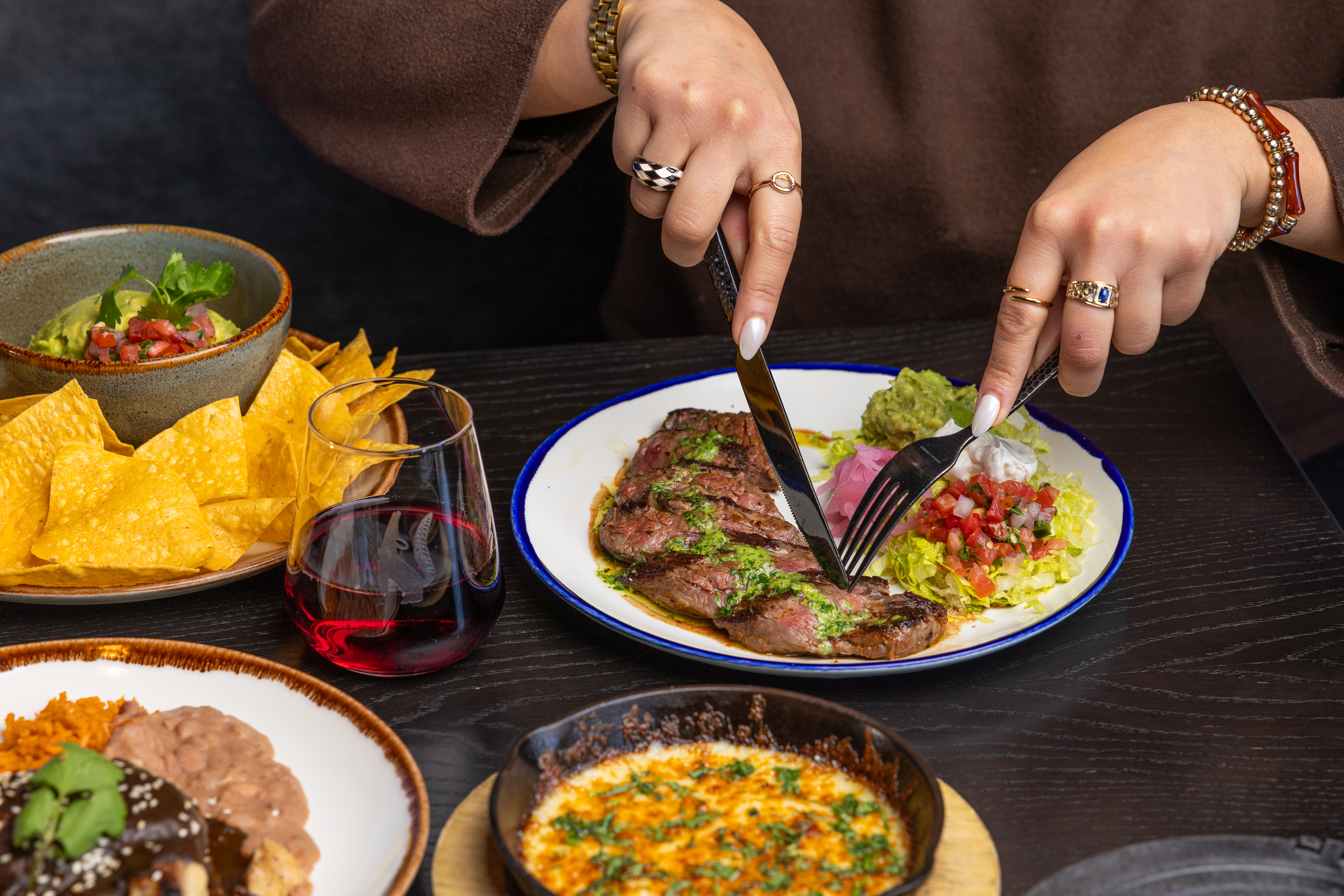 Assorted Mexican food on a table. Person cutting into a steak.
