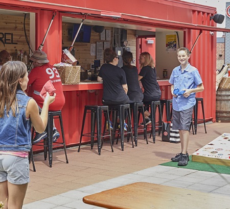 Kids playing corn hole outside, next to a beer garden.