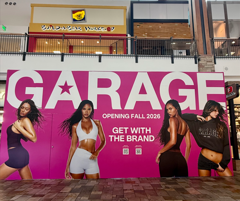 Large pink ‘Garage’ store opening banner featuring fashion models, with Build-A-Bear Workshop visible above in a shopping mall.
