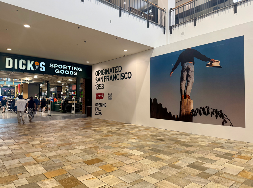 Mall storefront hoarding announcing Levi’s opening in Fall 2026, featuring a large lifestyle image and signage reading “Originated San Francisco 1853” beside Dick’s Sporting Goods
