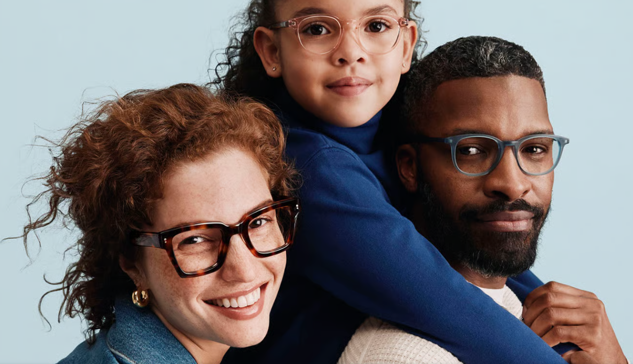 Three people wearing eyeglasses pose together against a light blue background, highlighting a variety of eyewear styles and frame designs.