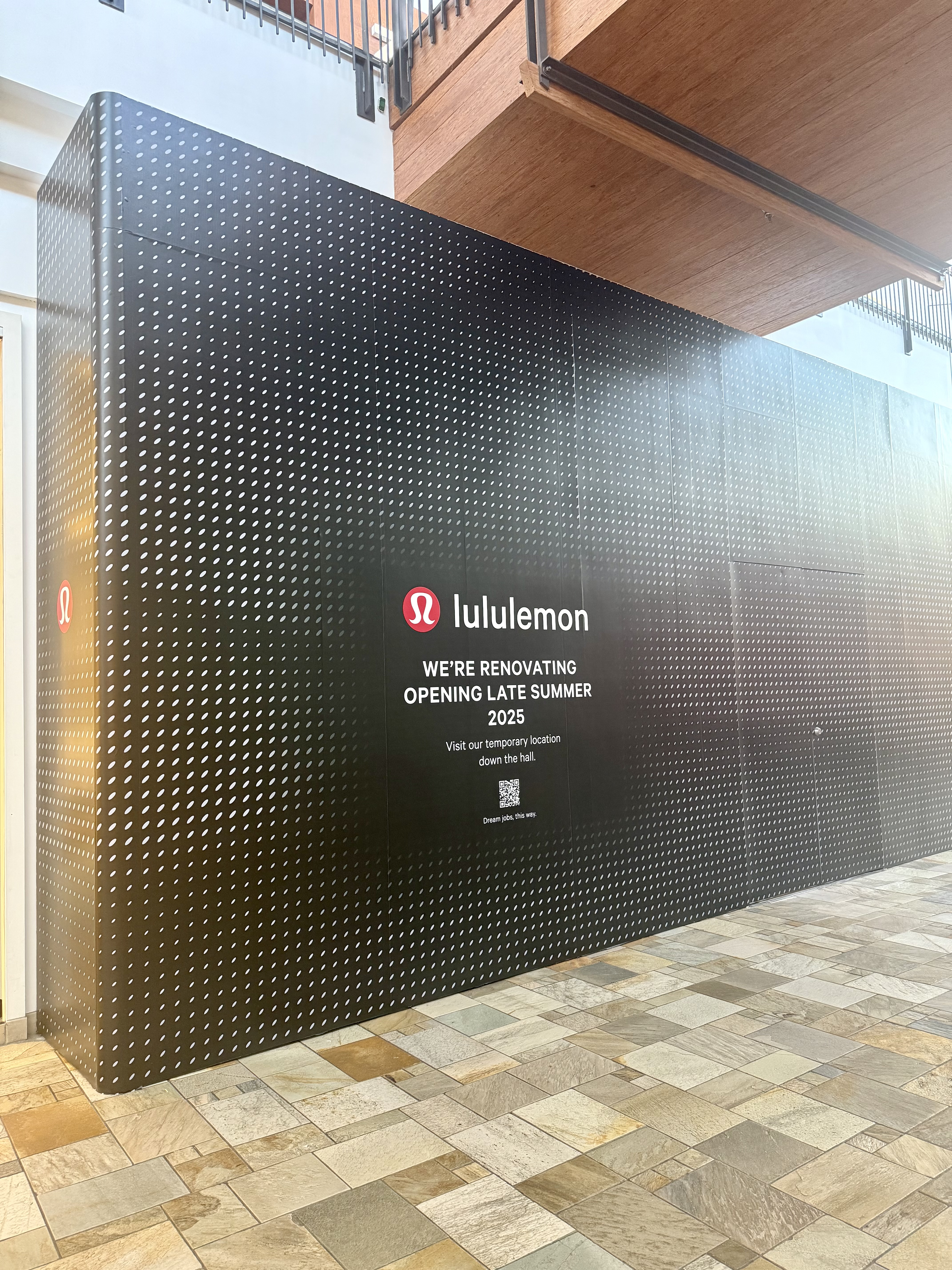 Black with white polka-dot store barricade with text reading "lululemon. we're renovating. opening late summer 2025. Visit our temporary location down the hall."