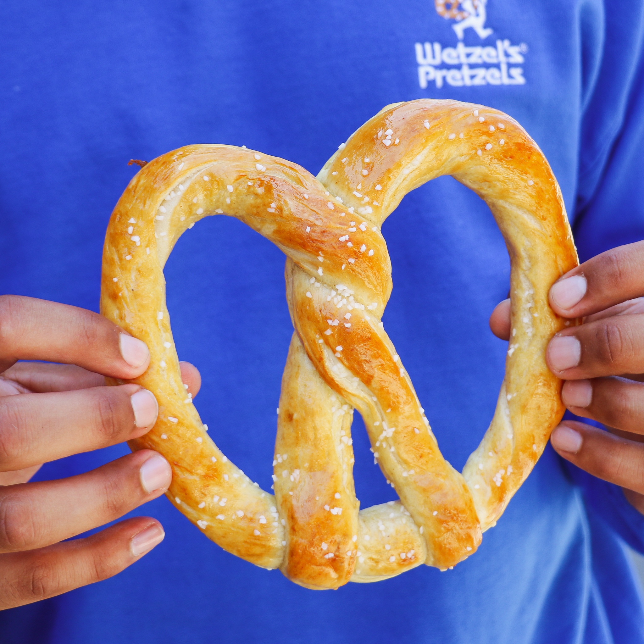 Person wearing a Wetzels Pretzel t-shirt holding a pretzel