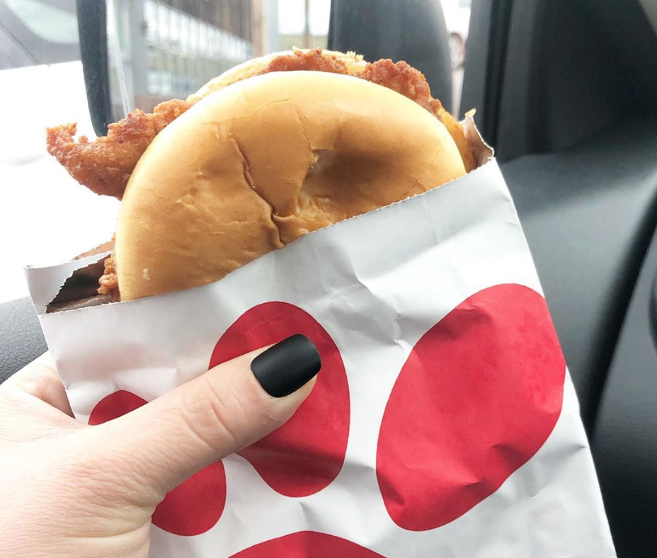 Woman's hand, with black nail polish, holding a Chick-fil-A chicken sandwich.
