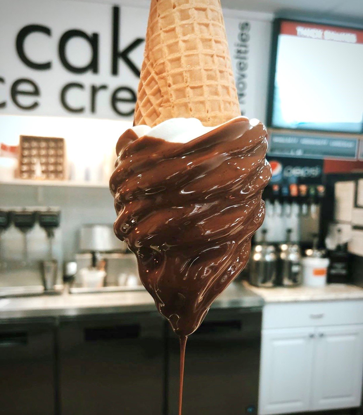 Upside down vanilla ice cream cone being dipped in chocolate
