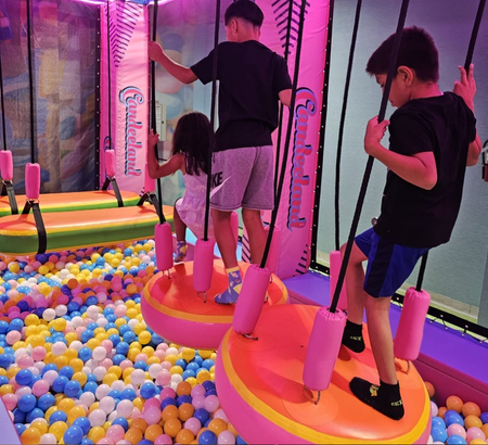 Three children on a ninja course over a ball pit