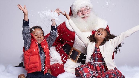 Santa Claus laughing with two children throwing snow in the air.
