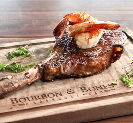 Tomahawk steak garnished with shrimp on a wooden chopping block.