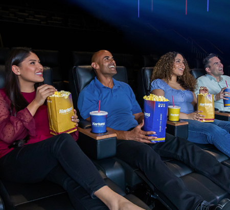 Moviegoers with popcorn and drinks smiling and looking at the screen.
