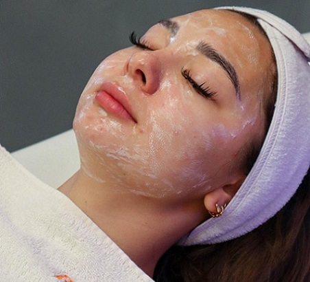 Woman receiving a facial with product on her face and a towel holding her hair back.