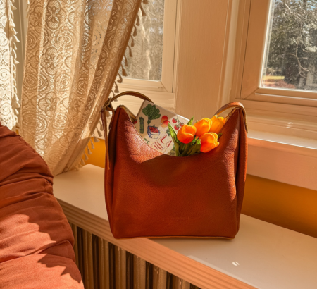 A leather purse filled with orange tulips and a book in a window sill.