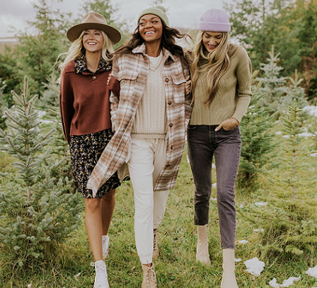 3 women wearing winter clothing and accessories walking through a field together smiling. 