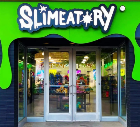 Storefront of a business with black brick and a sign that says Slimeatory with green oozing slime effect in the background.