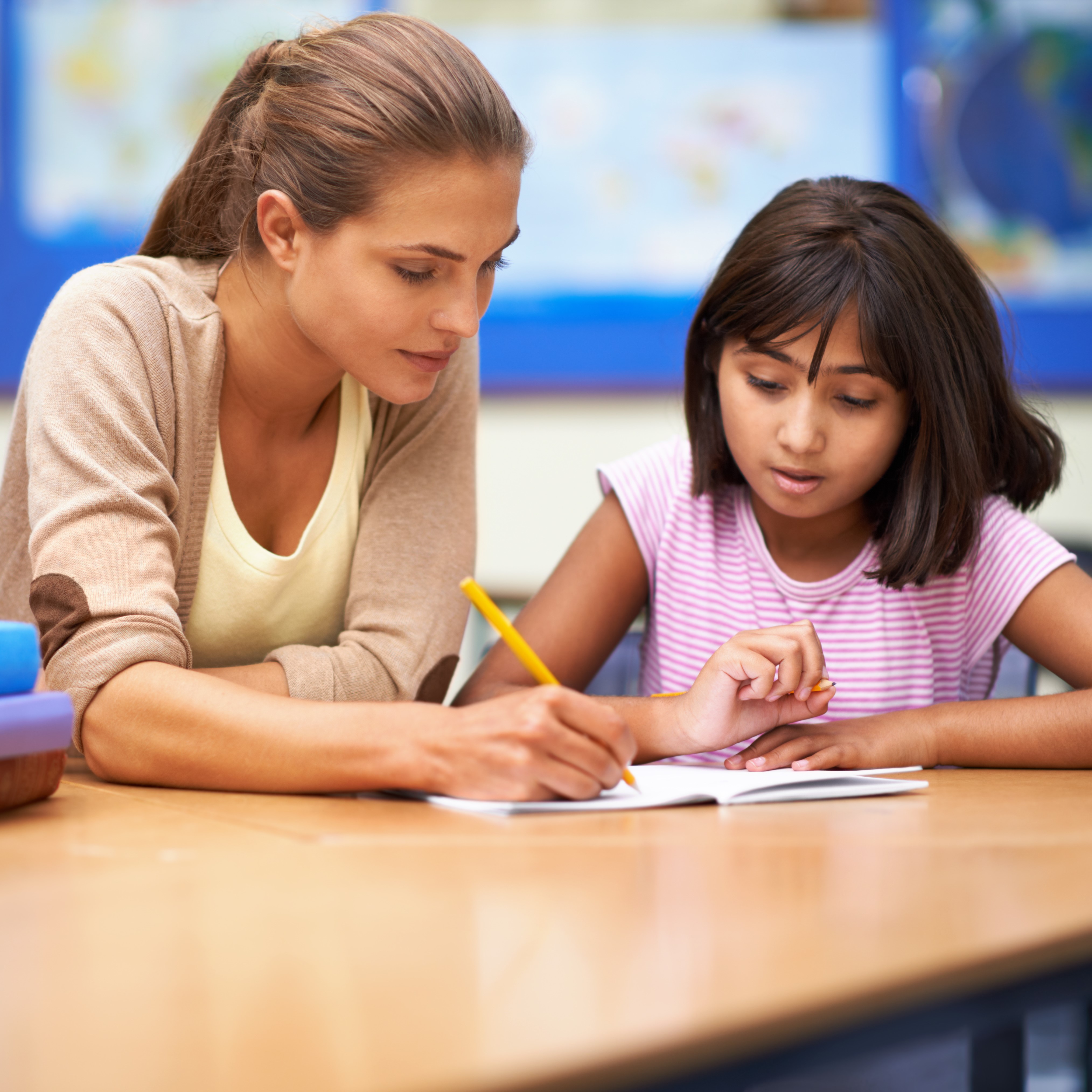 A teacher holding apencil going over a sheet of paper with a school-age girl.