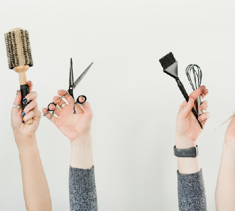 Hands holding a hair brush, sheers, and hair coloring tools.