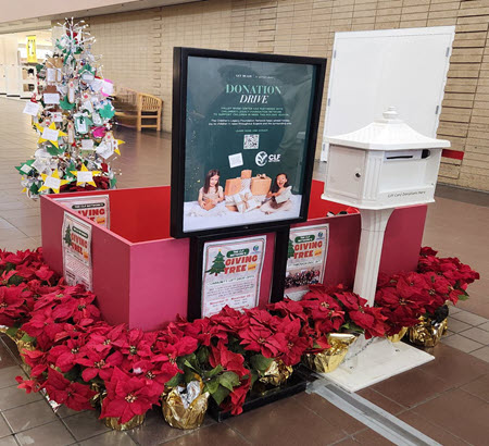A tree with ornaments next to a red donation box, a donation sign, and a mailbox.