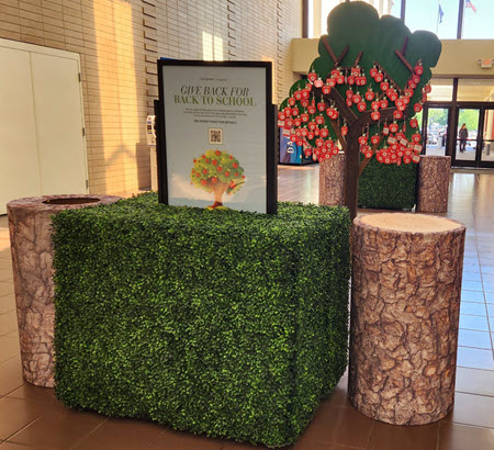 A few green hedges, lined with donation bins decorated like tree stumps, followed by a wooden apple tree.