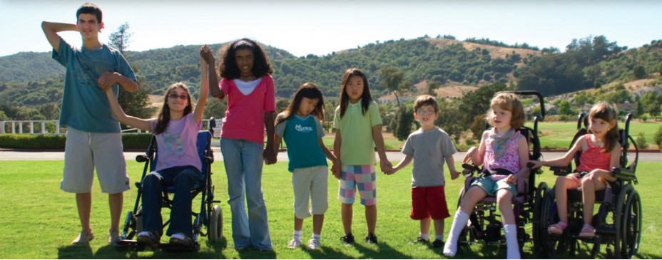 A group of children on the grass, holding hands. Some are in wheelchairs