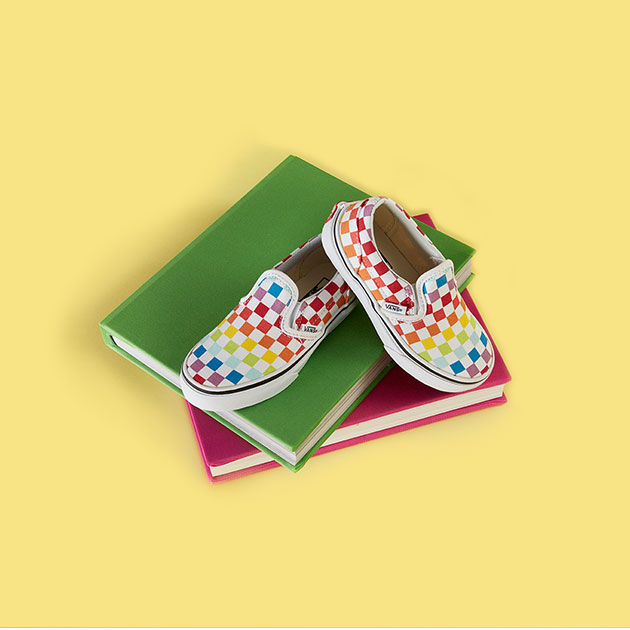 Pair of rainbow checkerboard Vans shoes on a stack of books
