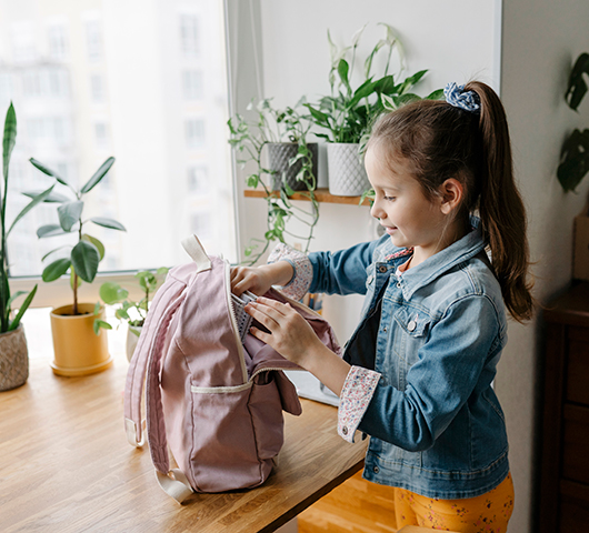 A school-age girl packing a backpack