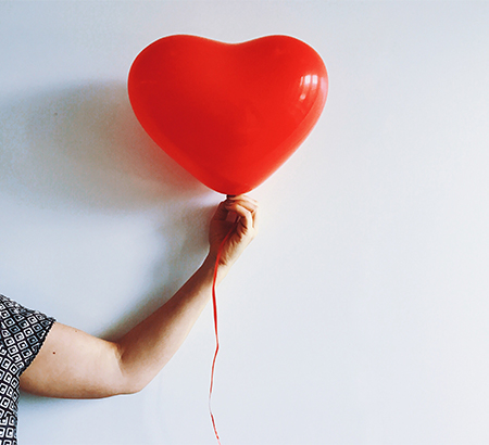 hand holding a red heart balloon