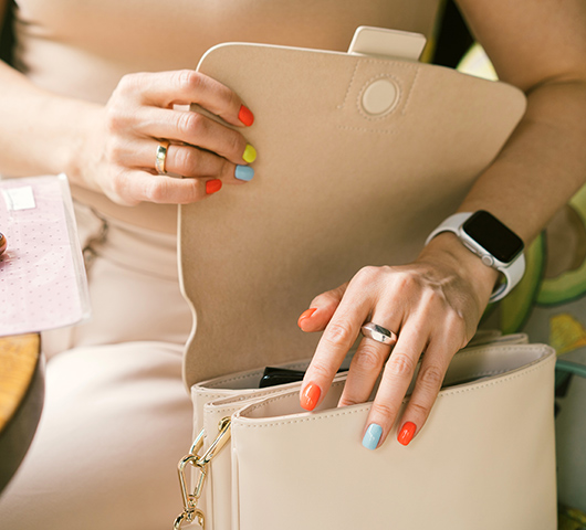 A woman with multicolored painted fingernails opening a white purse