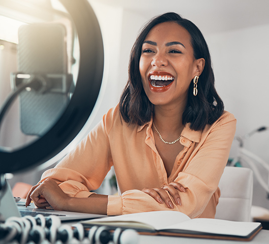 A woman recording on her phone at a desk with a ring light