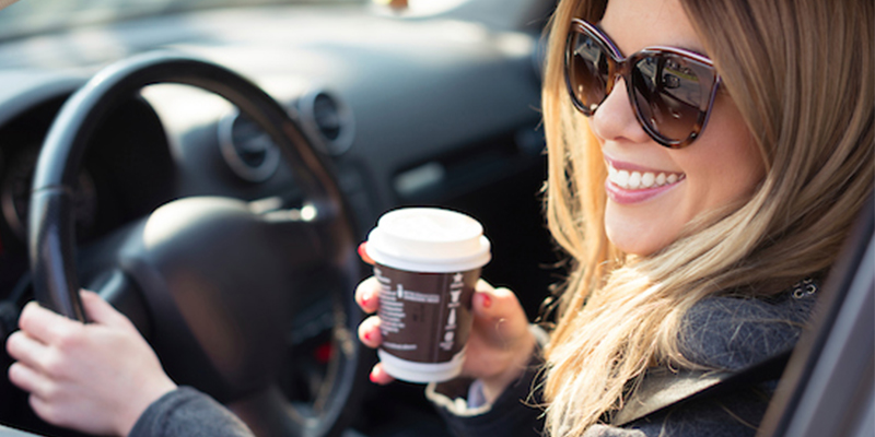 Smiling woman behind the wheel holding a coffee