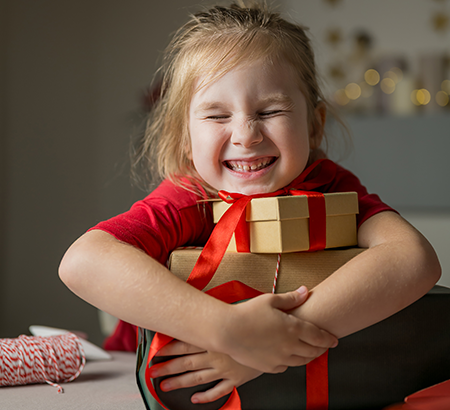 happy little girl wrapping arms around holiday gifts