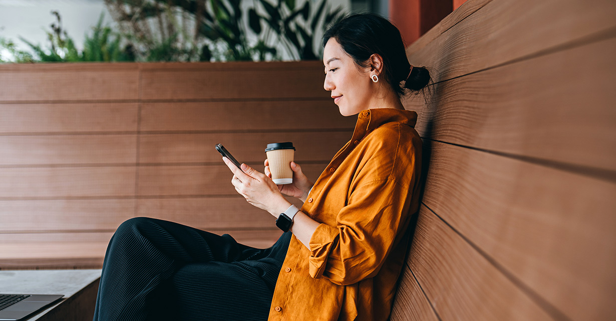 A woman looking at her phone and drinking a coffee