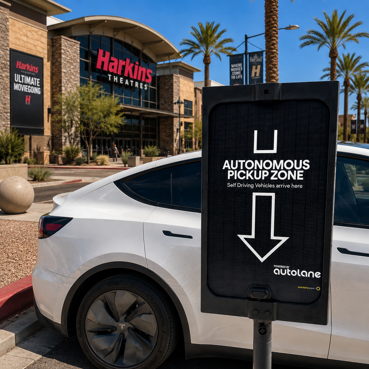 a tesla parked outside Harkins Theatres next to sign that says "Autonomous Pickup Zone, Self Driving Vehicles arrive here, powered by Autolane"