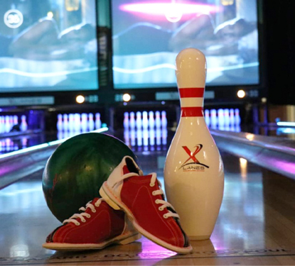 Bowling ball, pin, and shoes in front of a colorful bowling lane.