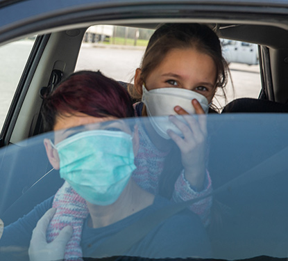 Two teens in masks inside a car awaiting a COVID test
