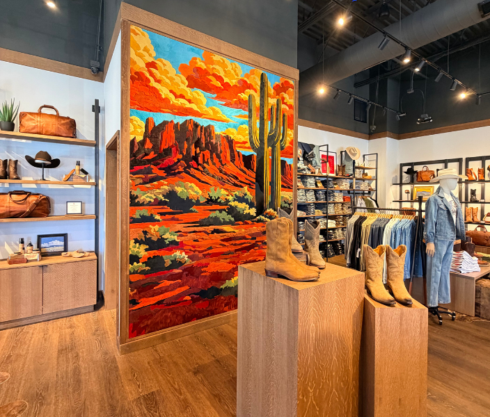 Tecovas sales floor displaying a colorful desert mural and shelves of apparel including boots, hats, bags and denim. 