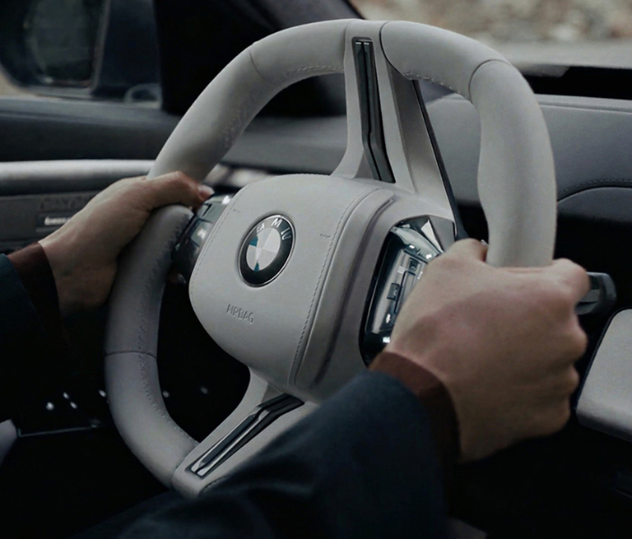 Hands steering a gray BMW steering wheel. 
