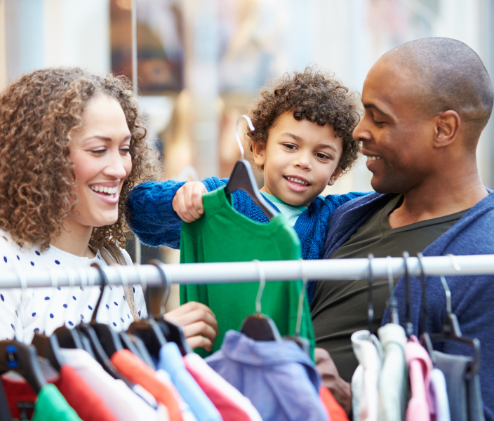 Man, woman and little boy smiling and looking at clothes on a rack. 