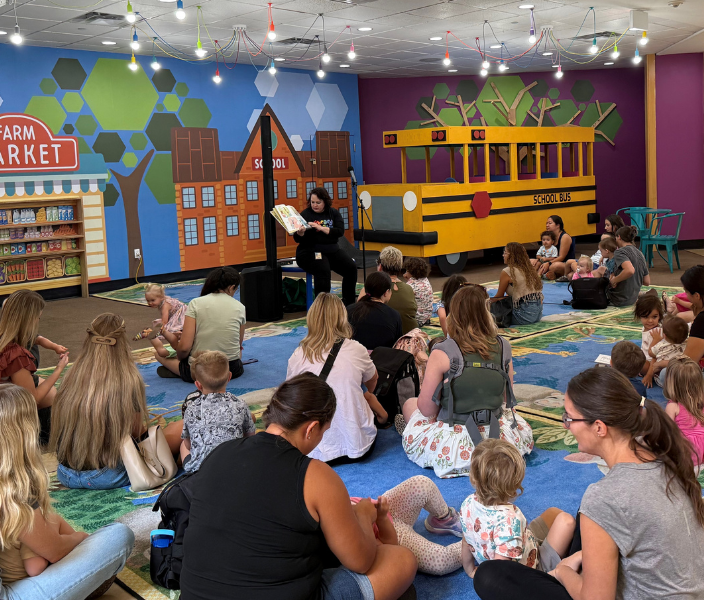 Parents and children sitting on rugs listening to a story being read. 