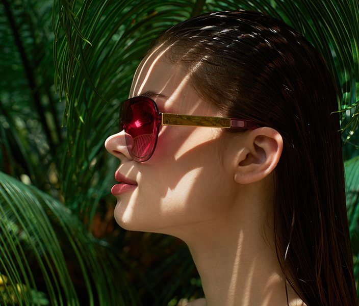 A female model pink sunglasses in front of palm fronds