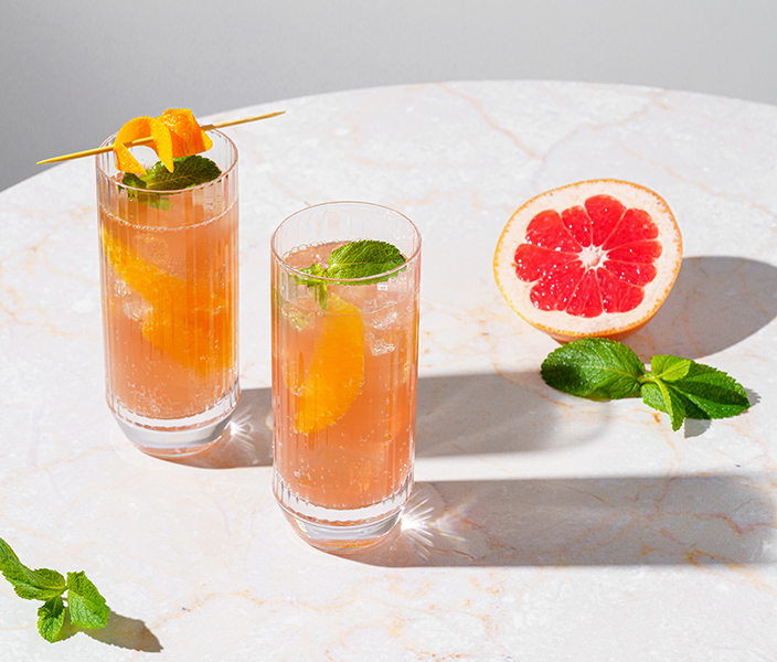 Two summer cocktails and half a grapefruit on a table
