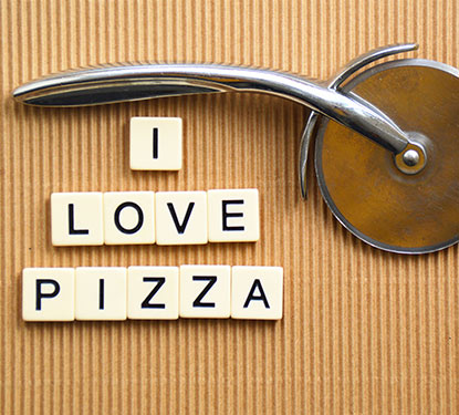 Scrabble letters spelling out "I Love Pizza" with a pizza cutter