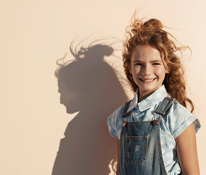 A preteen girl wearing overalls and a stylish shirt