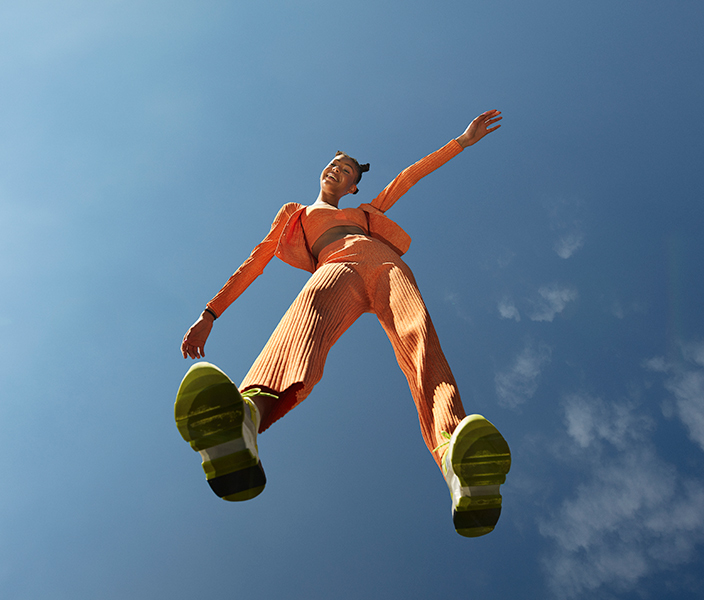 A young woman in sneakers and an orange track suit jumping up