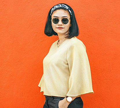 A stylish woman wearing sunglasses and standing in front of an orange wall